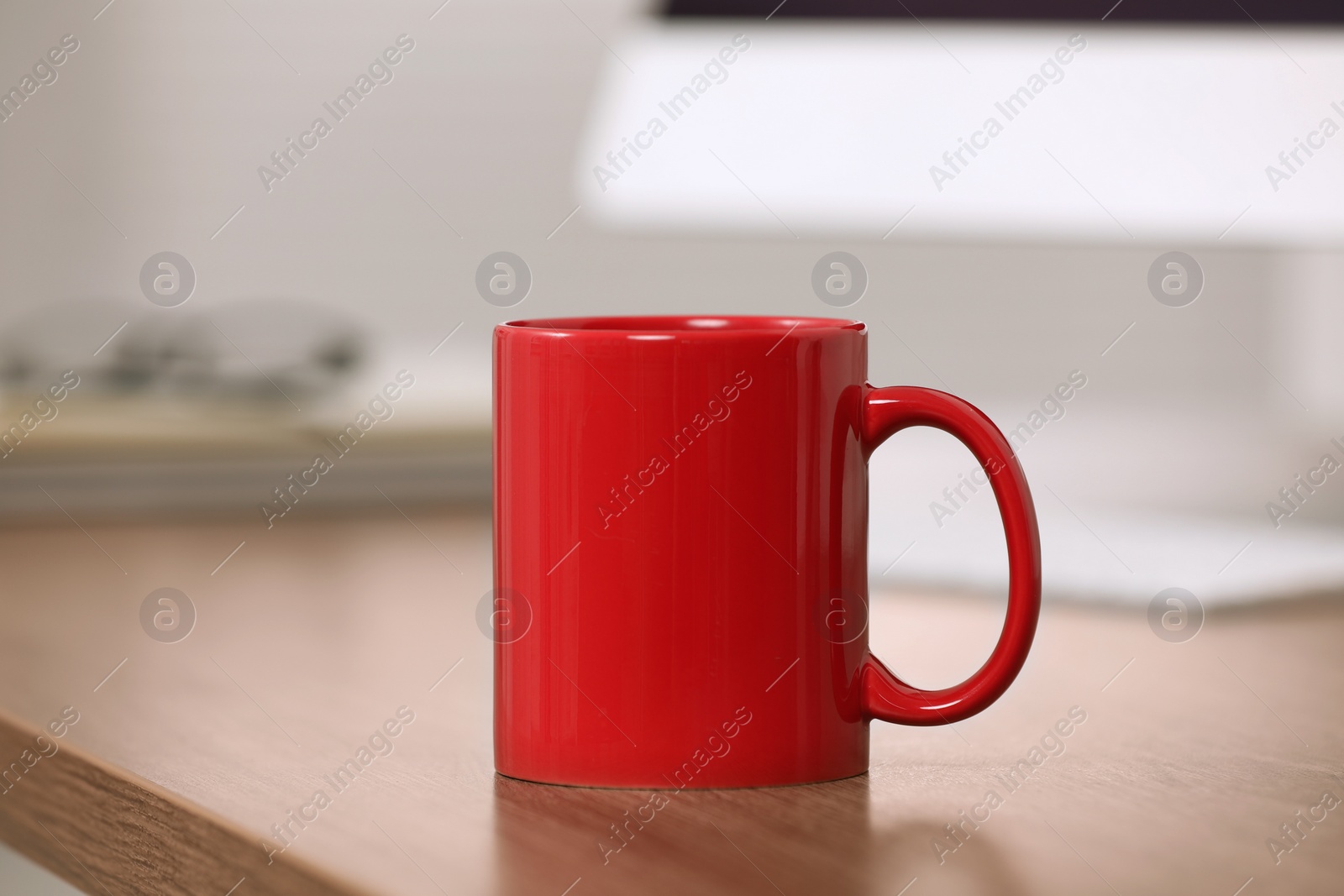 Photo of Red ceramic mug on wooden table at workplace