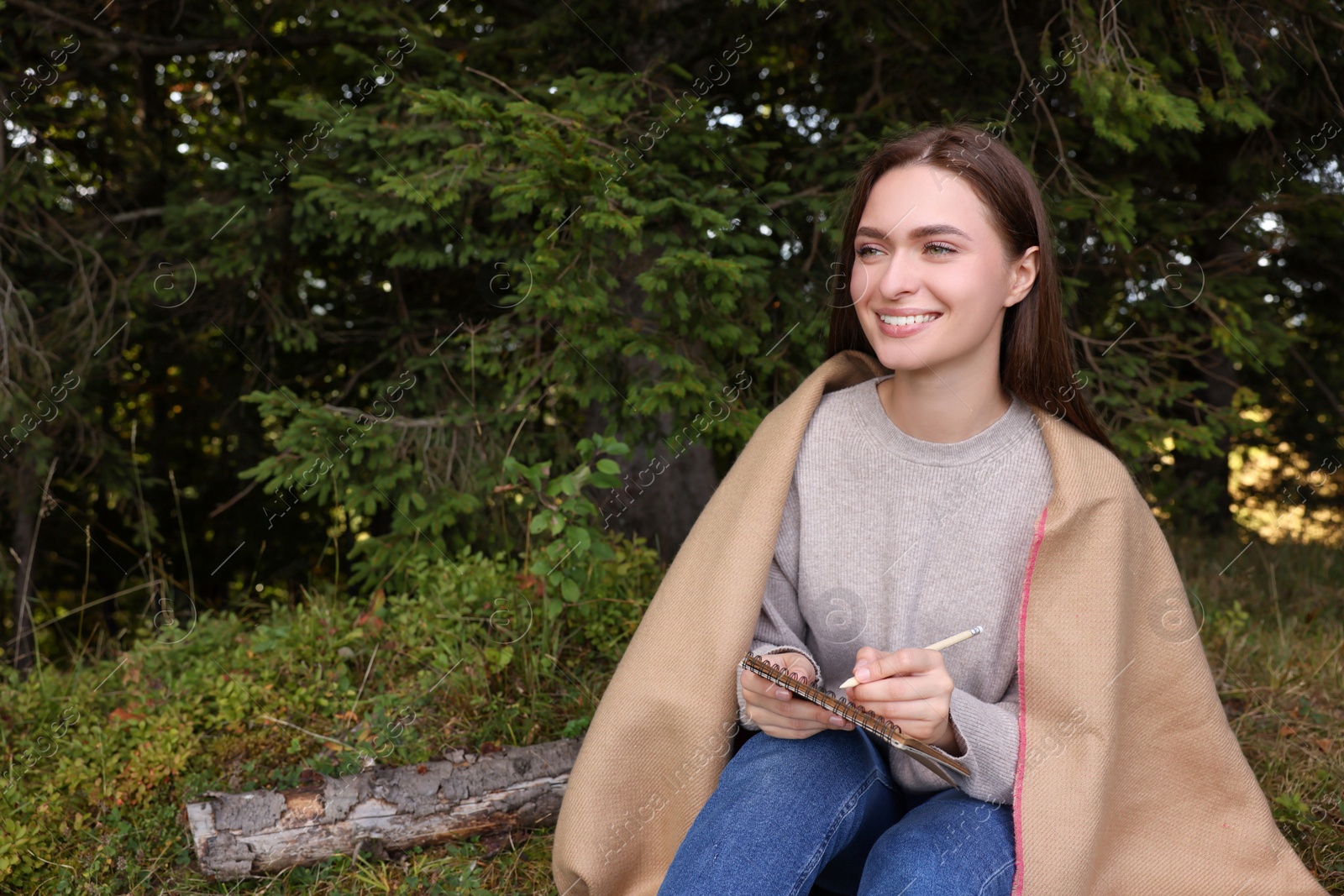 Photo of Young woman drawing with pencil in sketchbook near forest, space for text