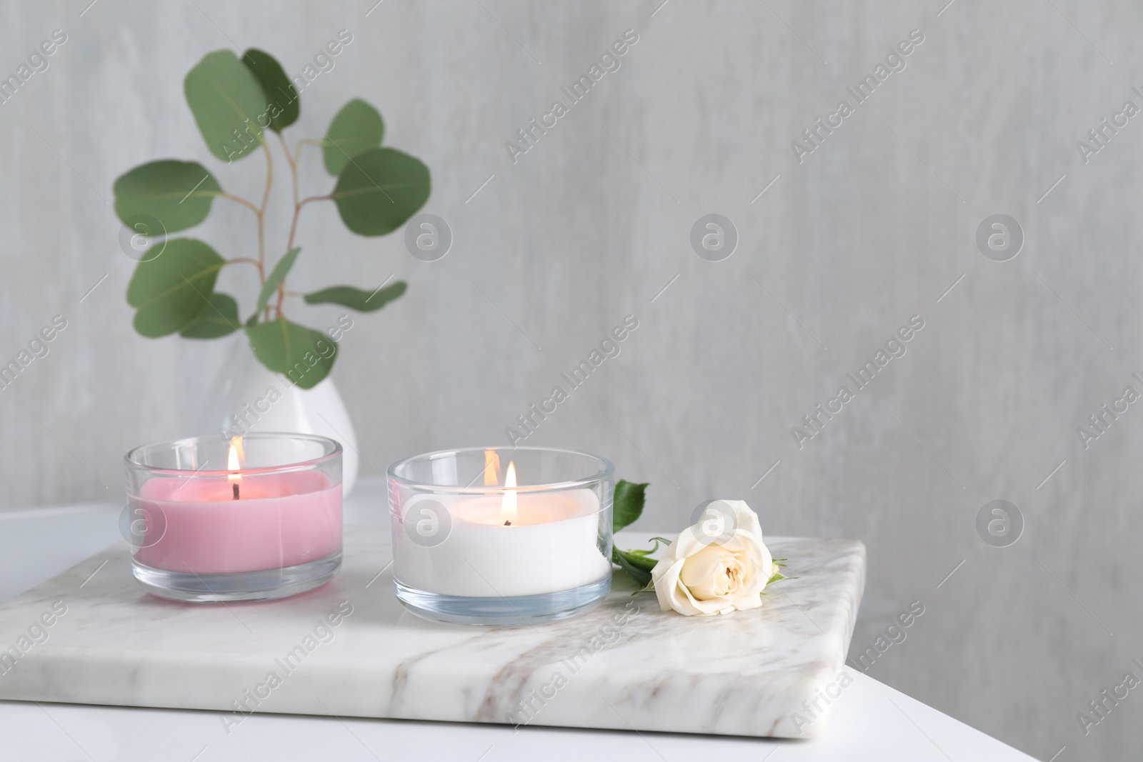 Photo of Burning candles and beautiful rose on white table