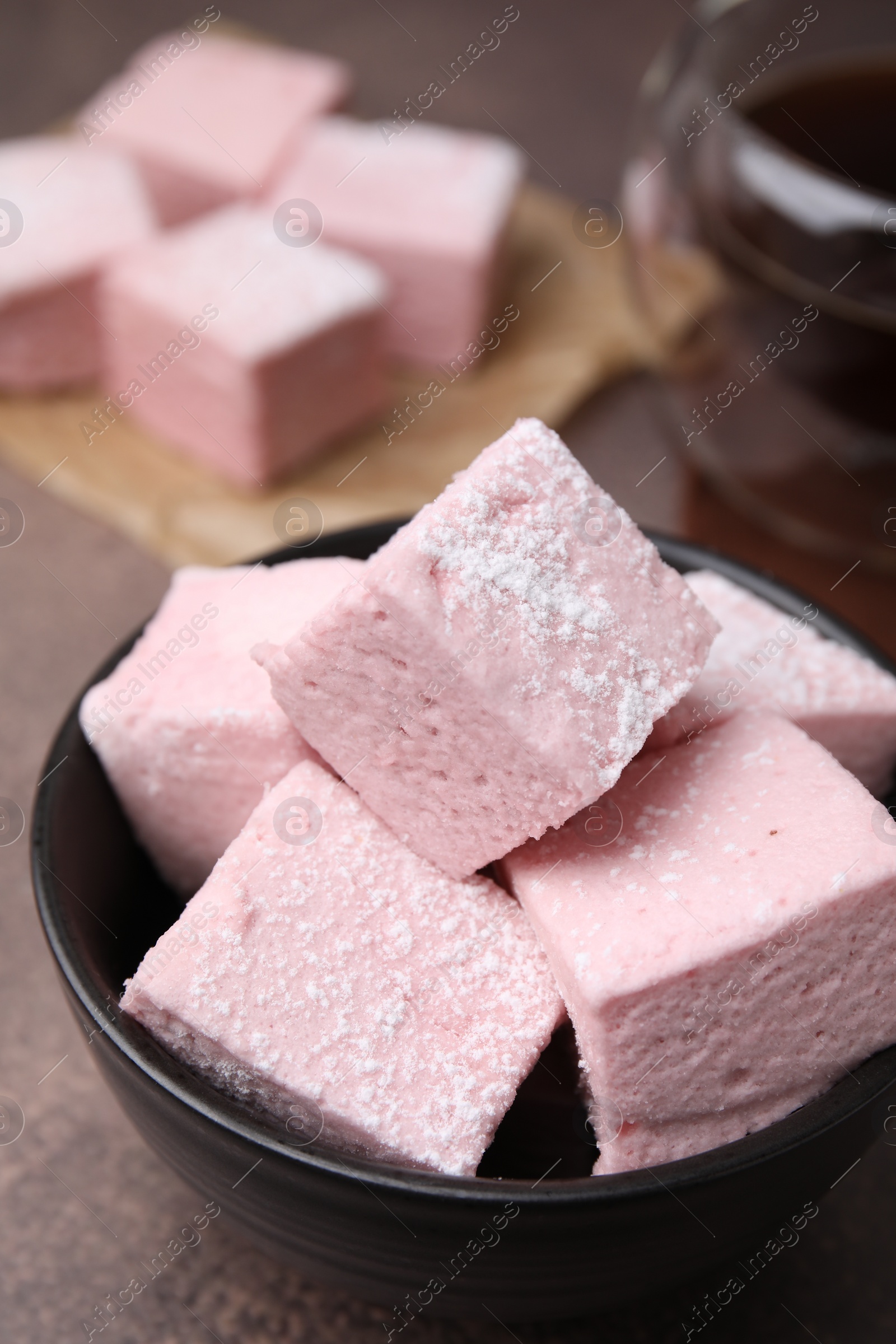 Photo of Bowl of delicious sweet marshmallows with powdered sugar on brown table, closeup