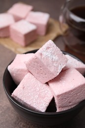 Bowl of delicious sweet marshmallows with powdered sugar on brown table, closeup