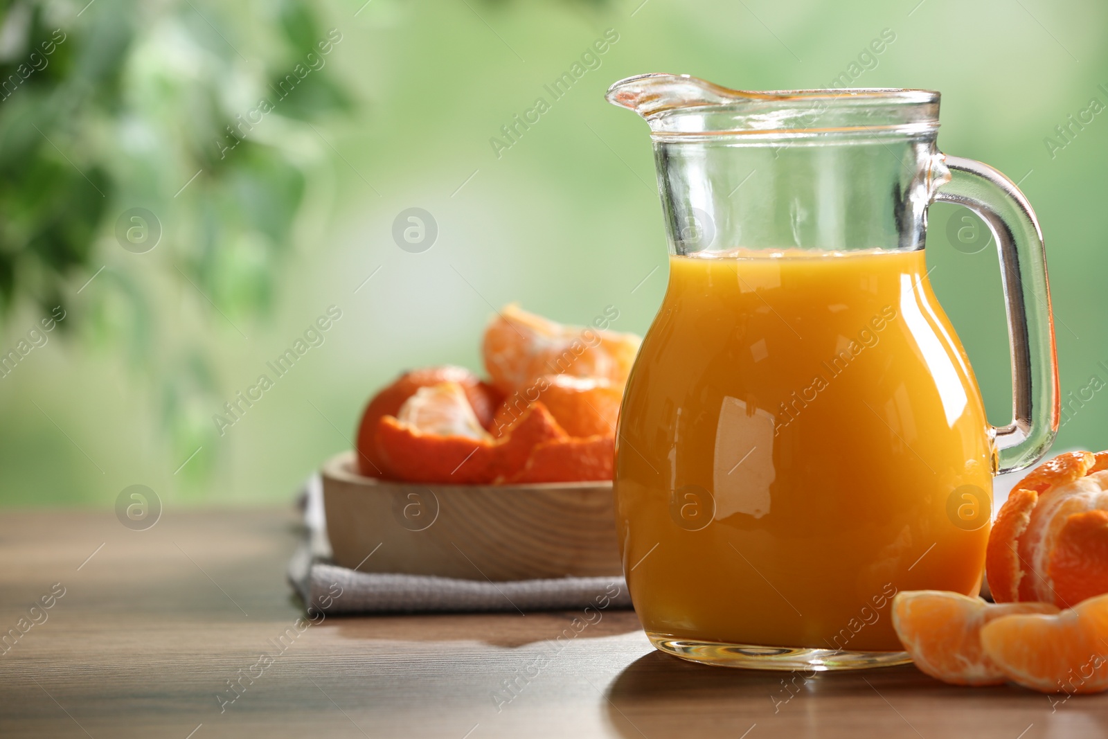 Photo of Delicious tangerine juice in jug and fresh fruits on wooden table against blurred background, space for text