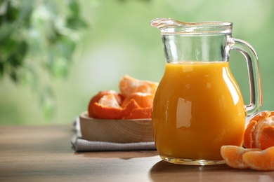 Photo of Delicious tangerine juice in jug and fresh fruits on wooden table against blurred background, space for text