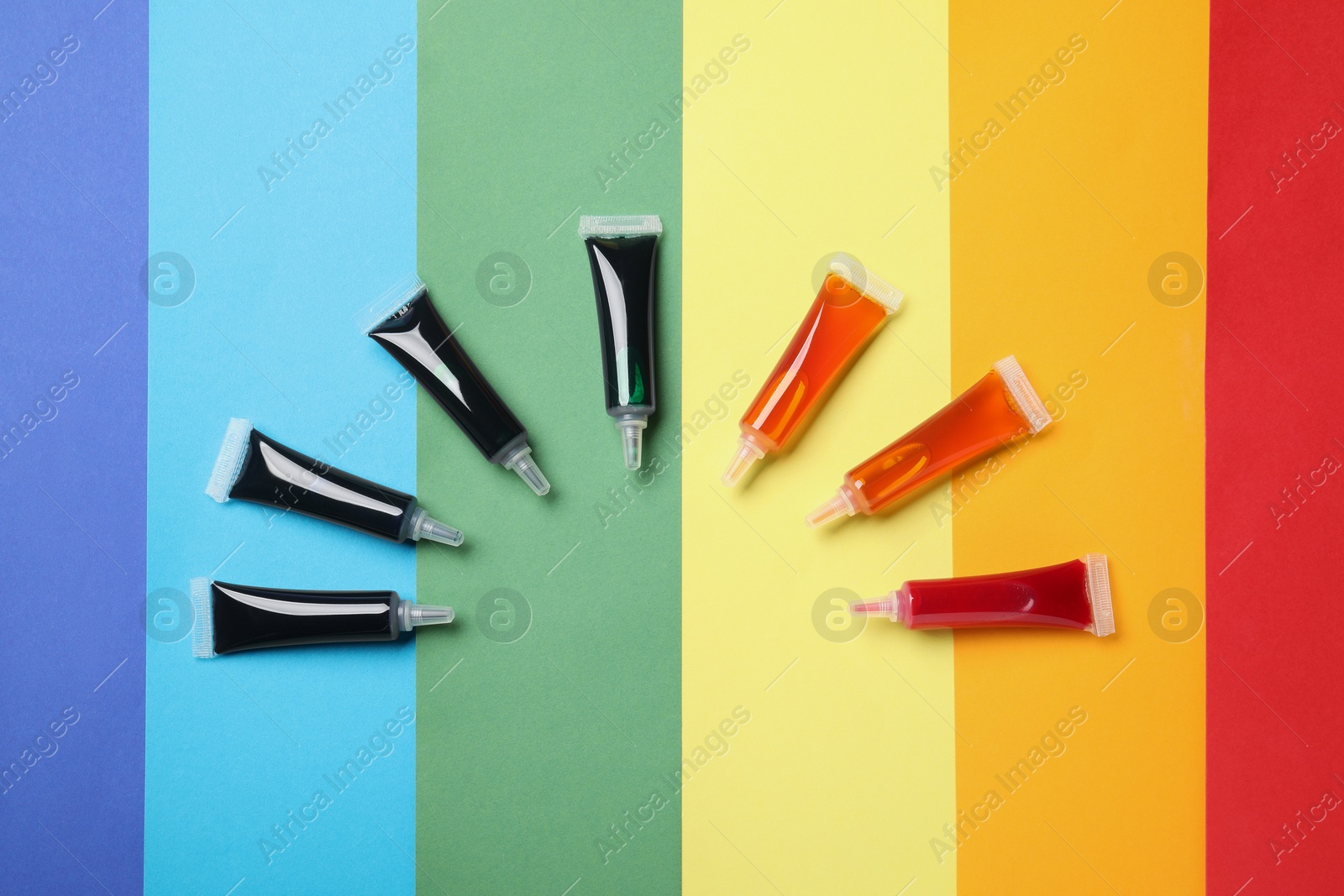 Photo of Tubes with different food coloring on rainbow background, flat lay