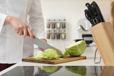 Professional chef cutting cabbage at white countertop in kitchen, closeup