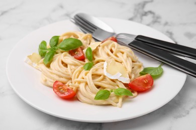 Photo of Delicious pasta with brie cheese, tomatoes, basil and cutlery on white marble table, closeup