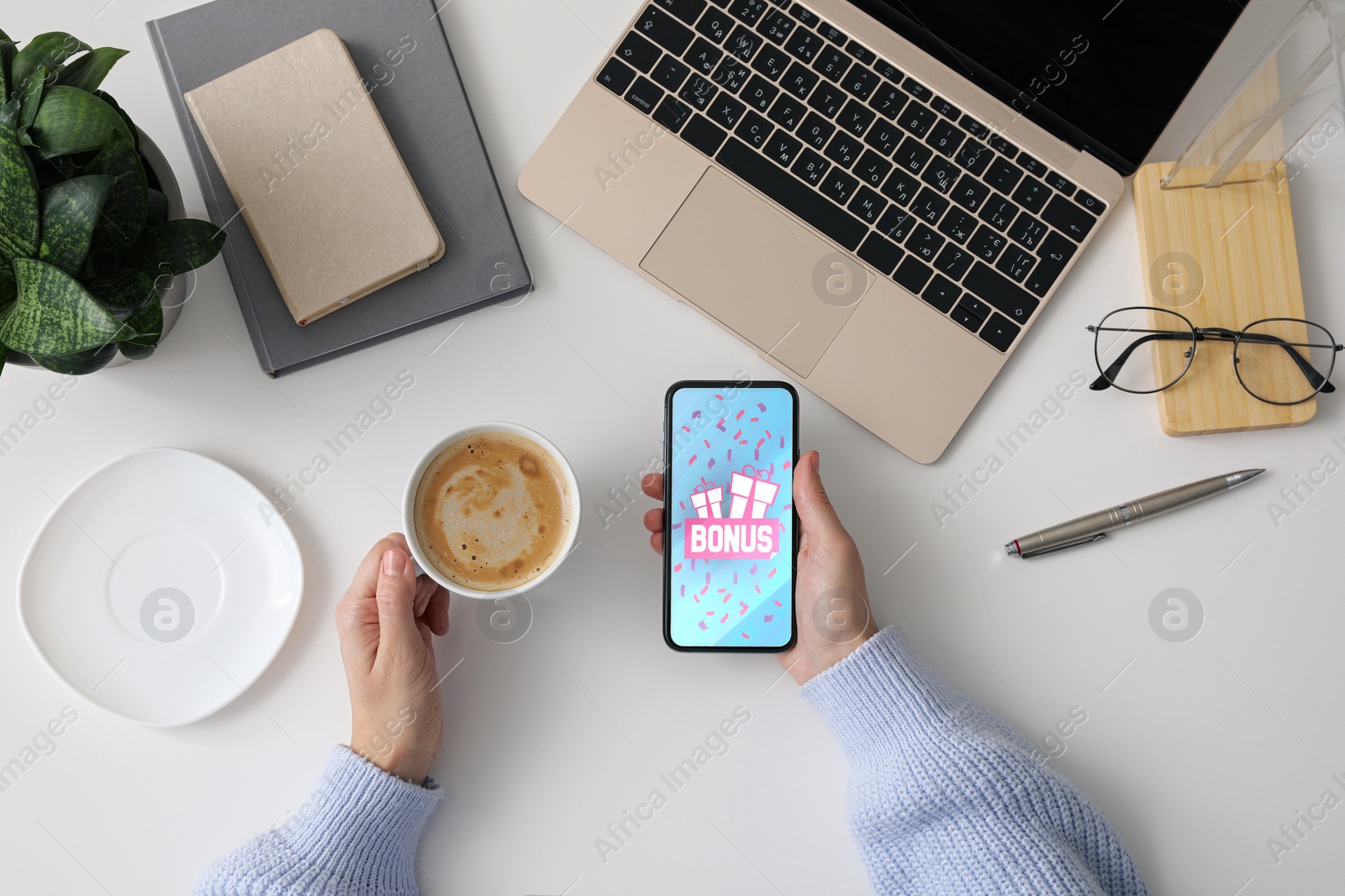 Image of Bonus gaining. Woman holding smartphone at white table, top view. Illustration of gift boxes, word and falling confetti on device screen