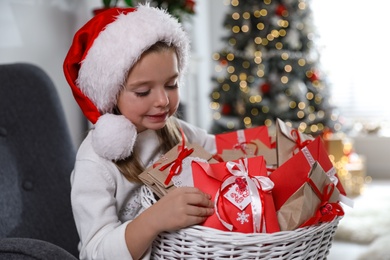 Cute little girl in Santa hat with gifts from Christmas advent calendar at home