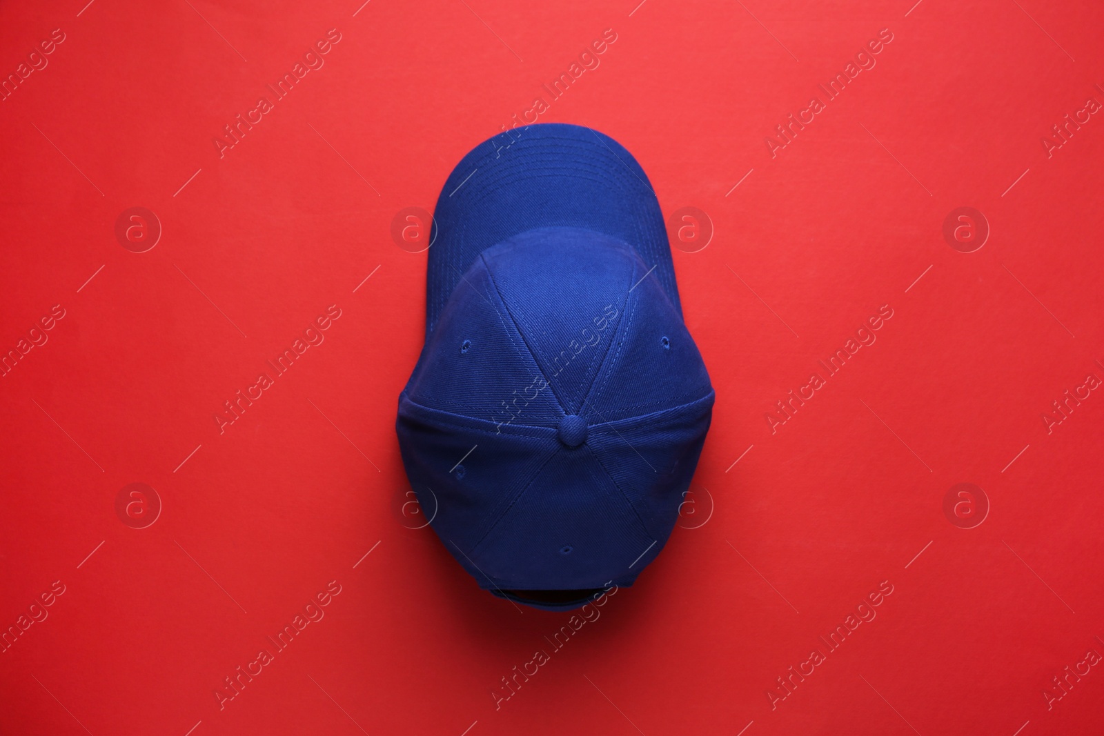 Photo of Stylish blue baseball cap on red background, top view