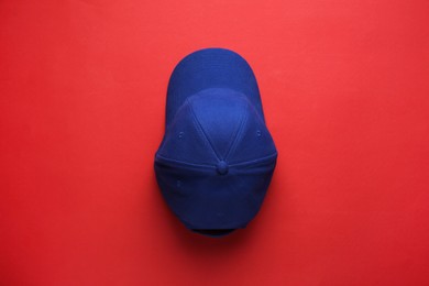 Photo of Stylish blue baseball cap on red background, top view