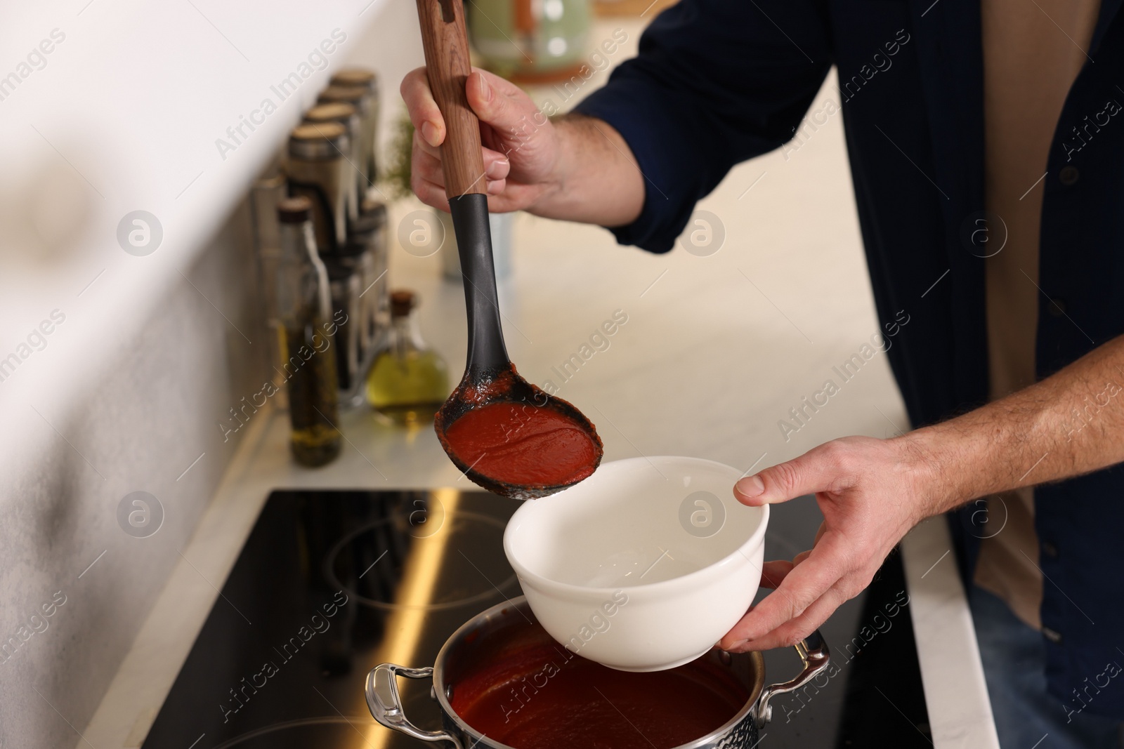 Photo of Man pouring delicious tomato soup into bowl in kitchen, closeup