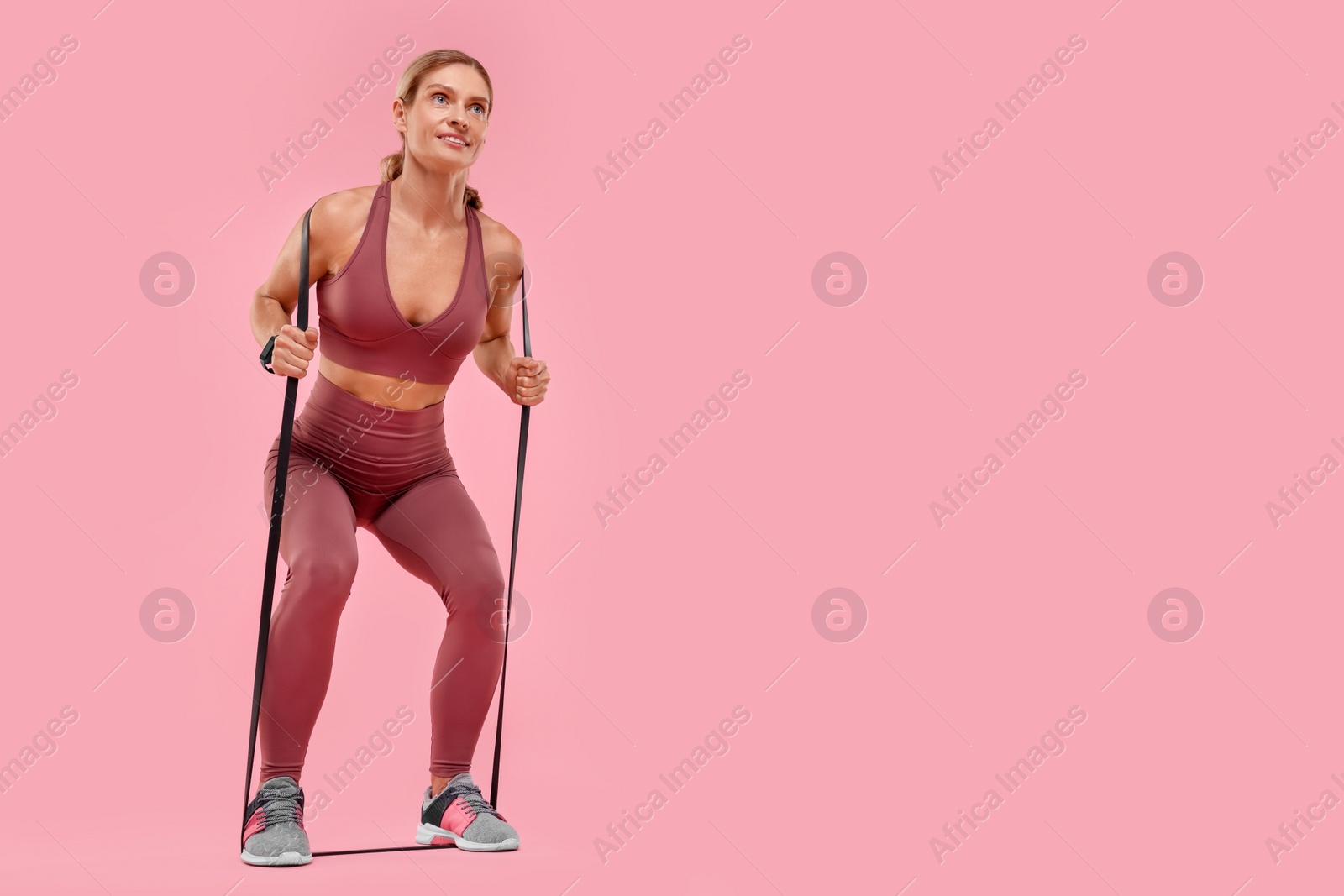 Photo of Woman exercising with elastic resistance band on pink background, low angle view. Space for text