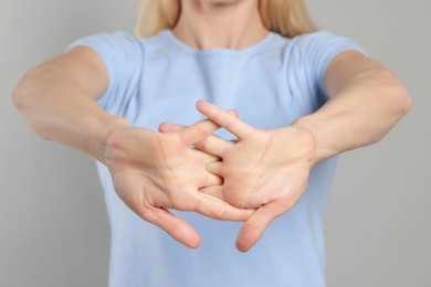 Woman cracking her knuckles on light grey background, closeup. Bad habit