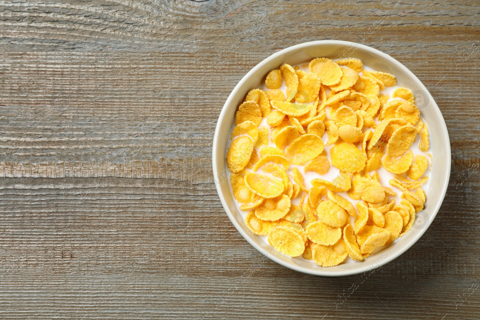 Photo of Tasty crispy corn flakes with milk on wooden  table, top view. Space for text