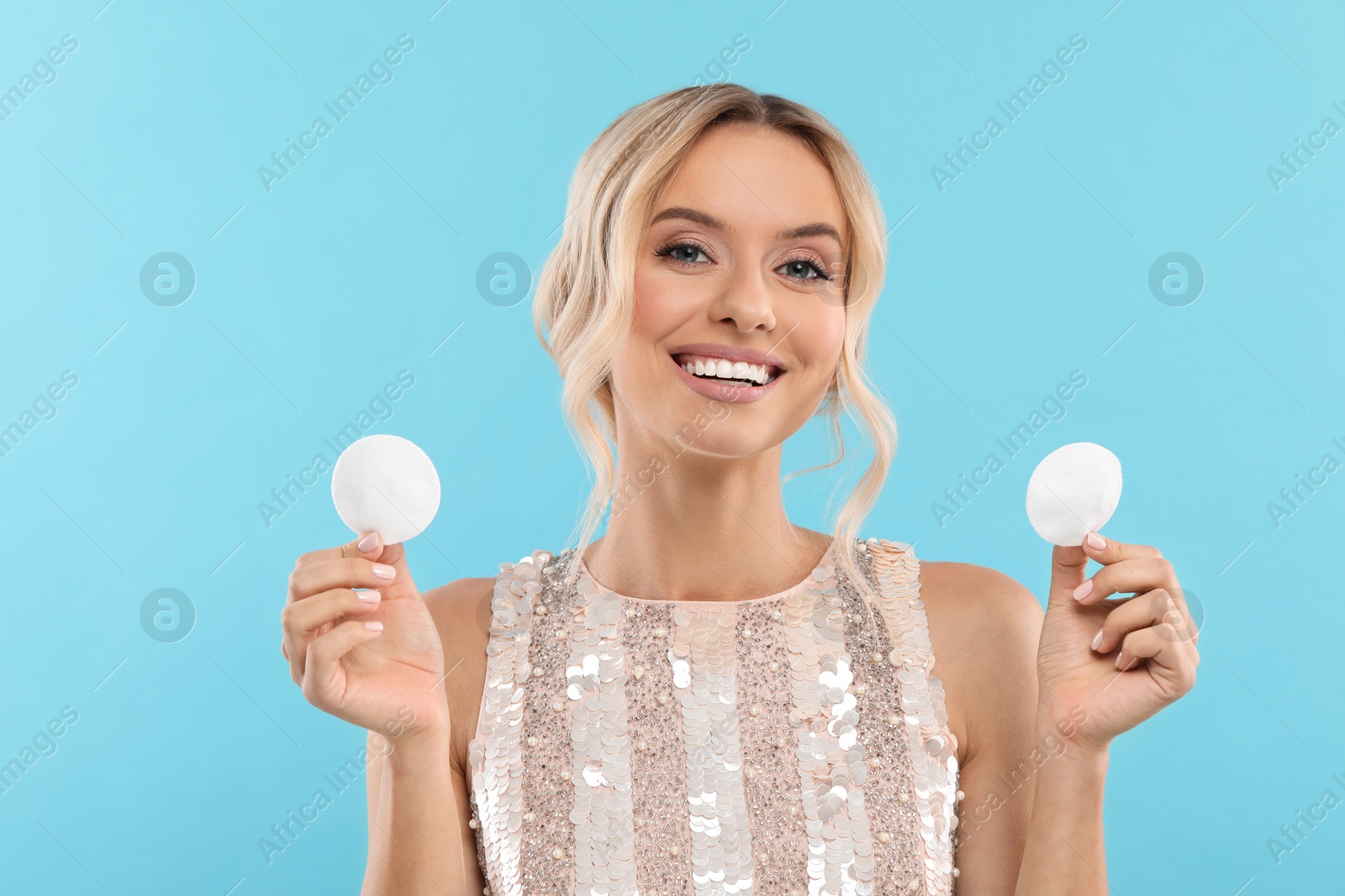 Photo of Removing makeup. Smiling woman with cotton pads on light blue background