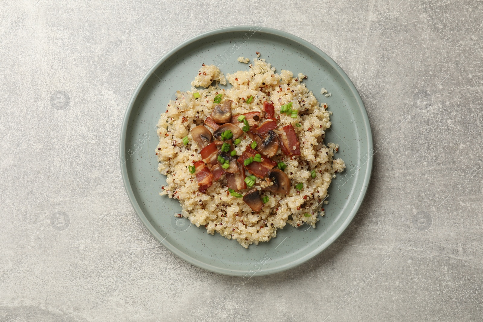 Photo of Plate of tasty quinoa porridge with fried bacon, mushrooms and green onion on light grey table, top view