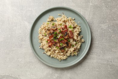 Photo of Plate of tasty quinoa porridge with fried bacon, mushrooms and green onion on light grey table, top view