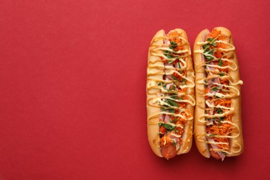 Photo of Delicious hot dogs with bacon, carrot and parsley on red background, top view. Space for text