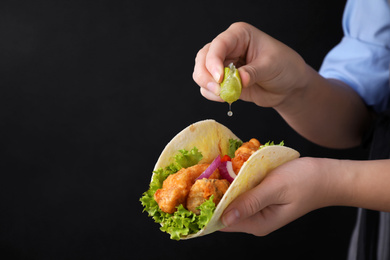 Photo of Woman squeezing lime on fish taco against dark background, closeup