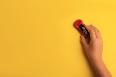 Photo of Child playing with toy car on yellow background, top view. Space for text