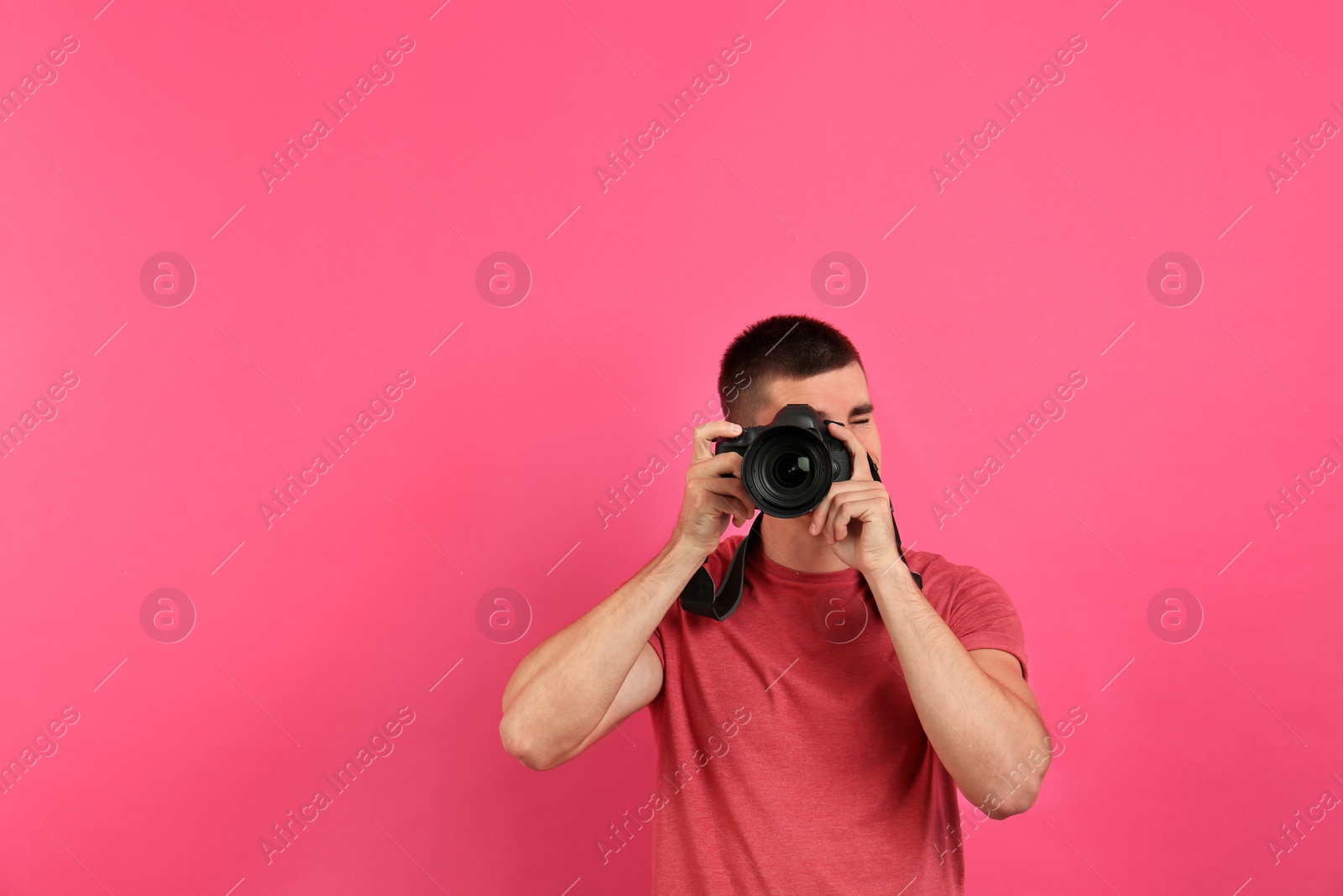 Photo of Young professional photographer taking picture on pink background. Space for text