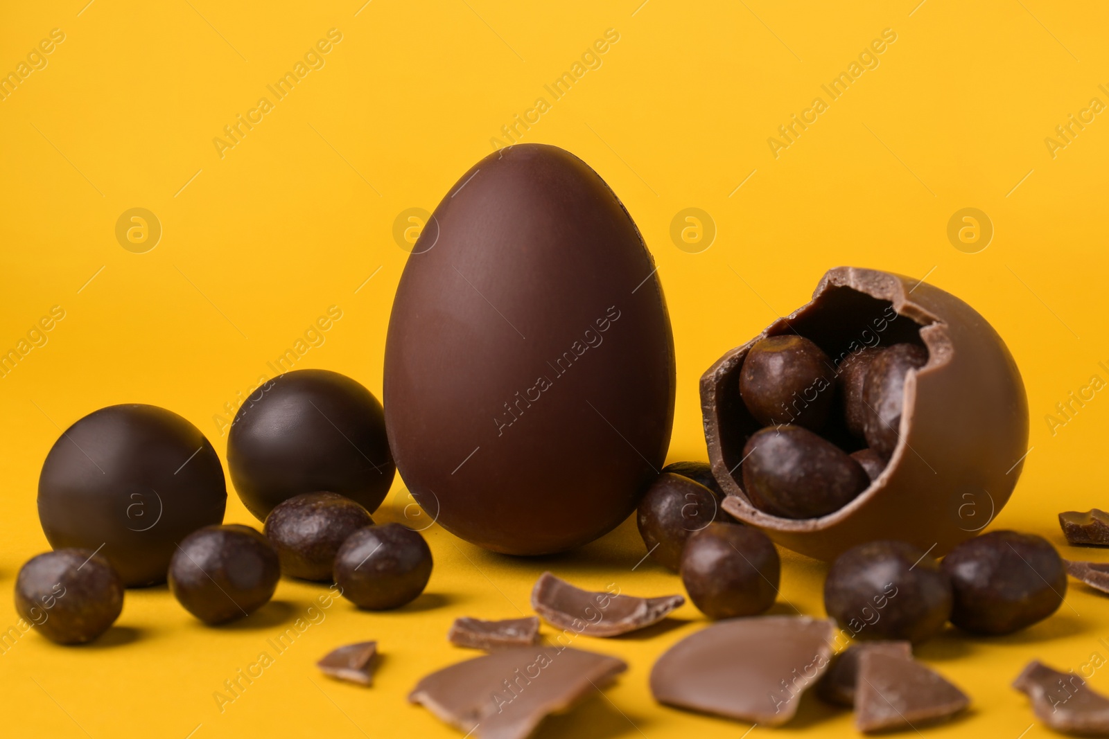 Photo of Tasty whole and broken chocolate eggs with candies on orange background