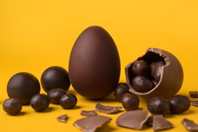 Photo of Tasty whole and broken chocolate eggs with candies on orange background