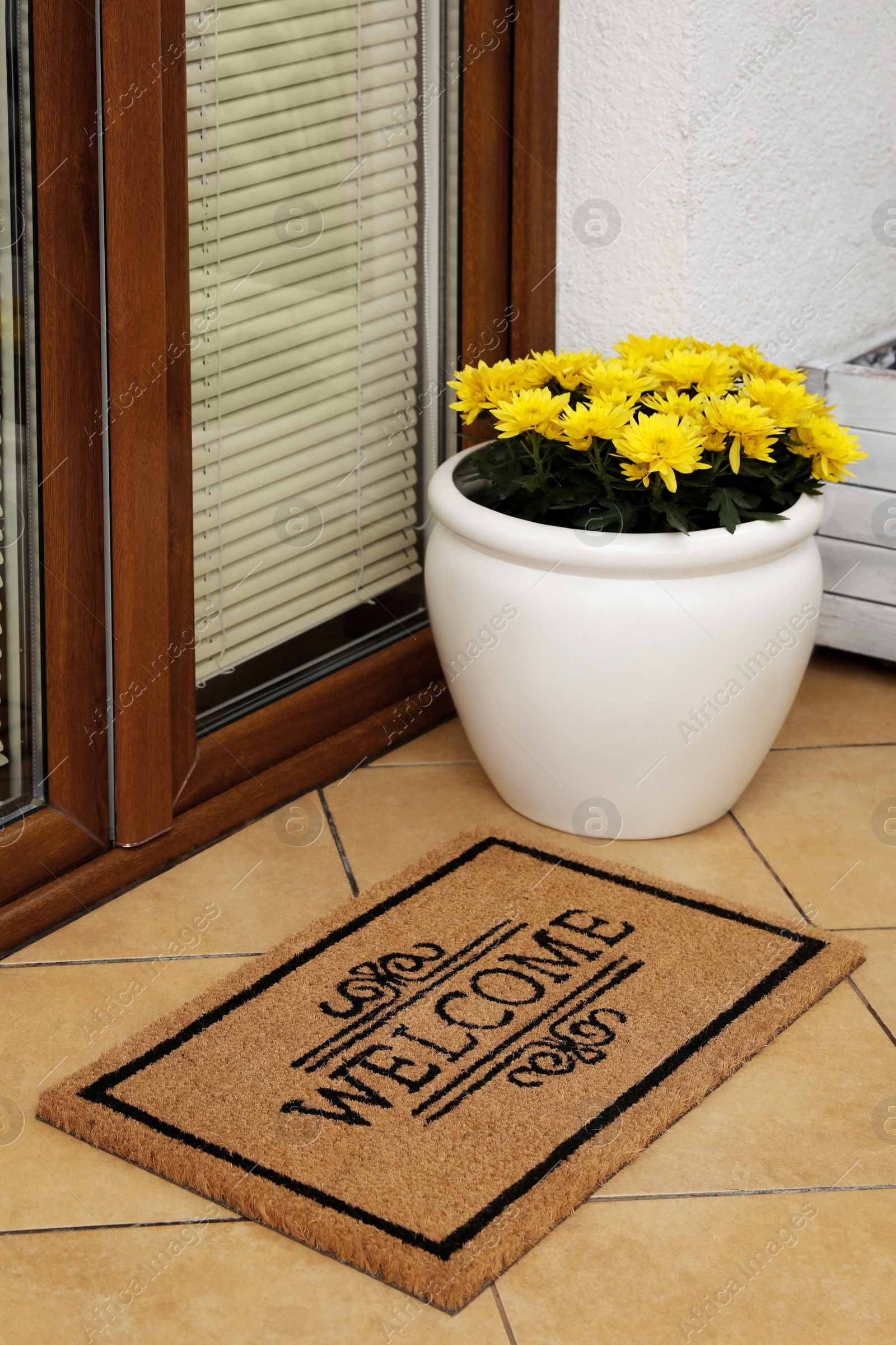 Photo of Door mat with word Welcome and beautiful flowers on floor near entrance