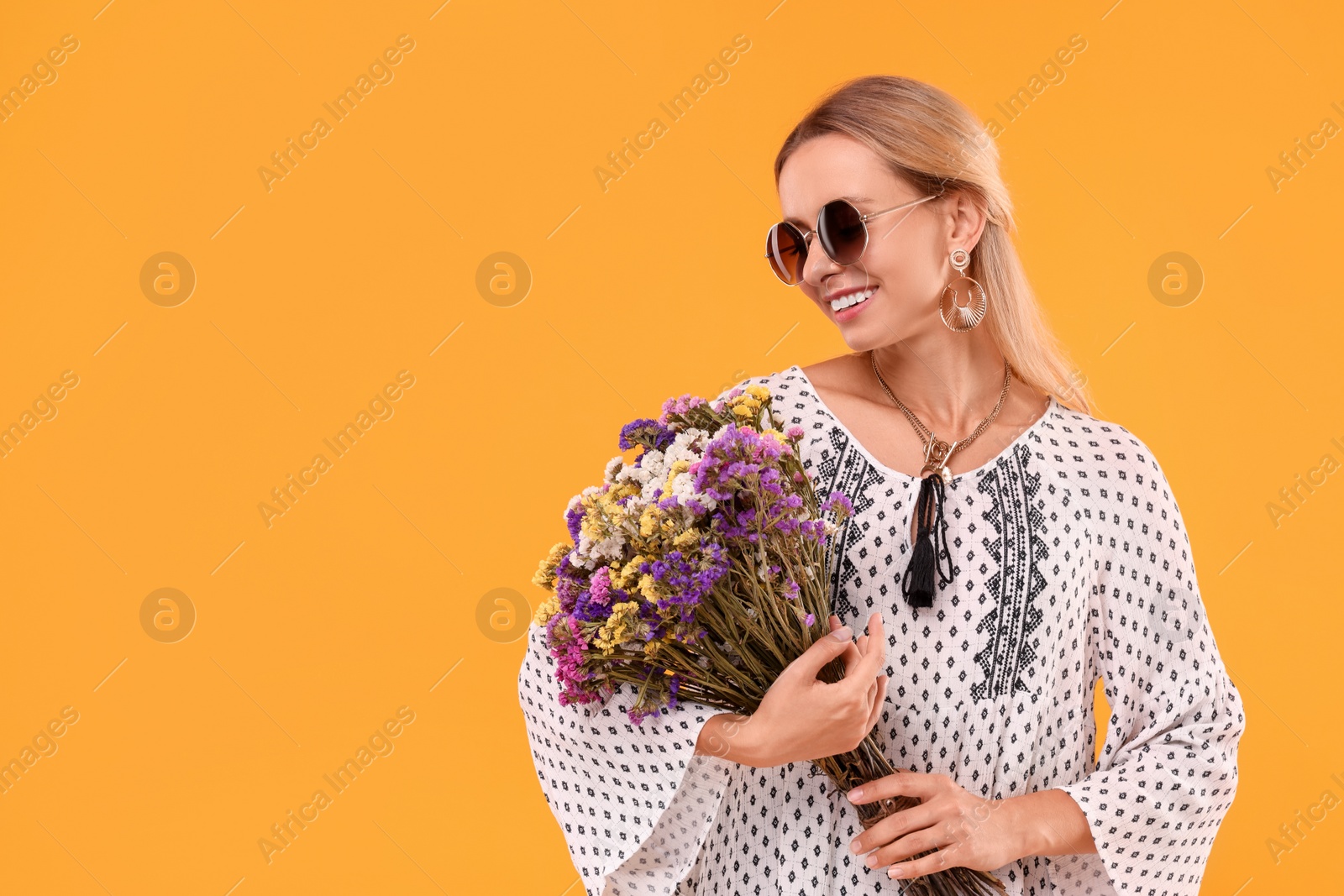 Photo of Portrait of smiling hippie woman with bouquet of flowers on yellow background. Space for text