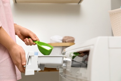 Photo of Woman pouring powder into drawer of washing machine in laundry room, closeup