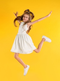 Photo of Cute little girl jumping on yellow background