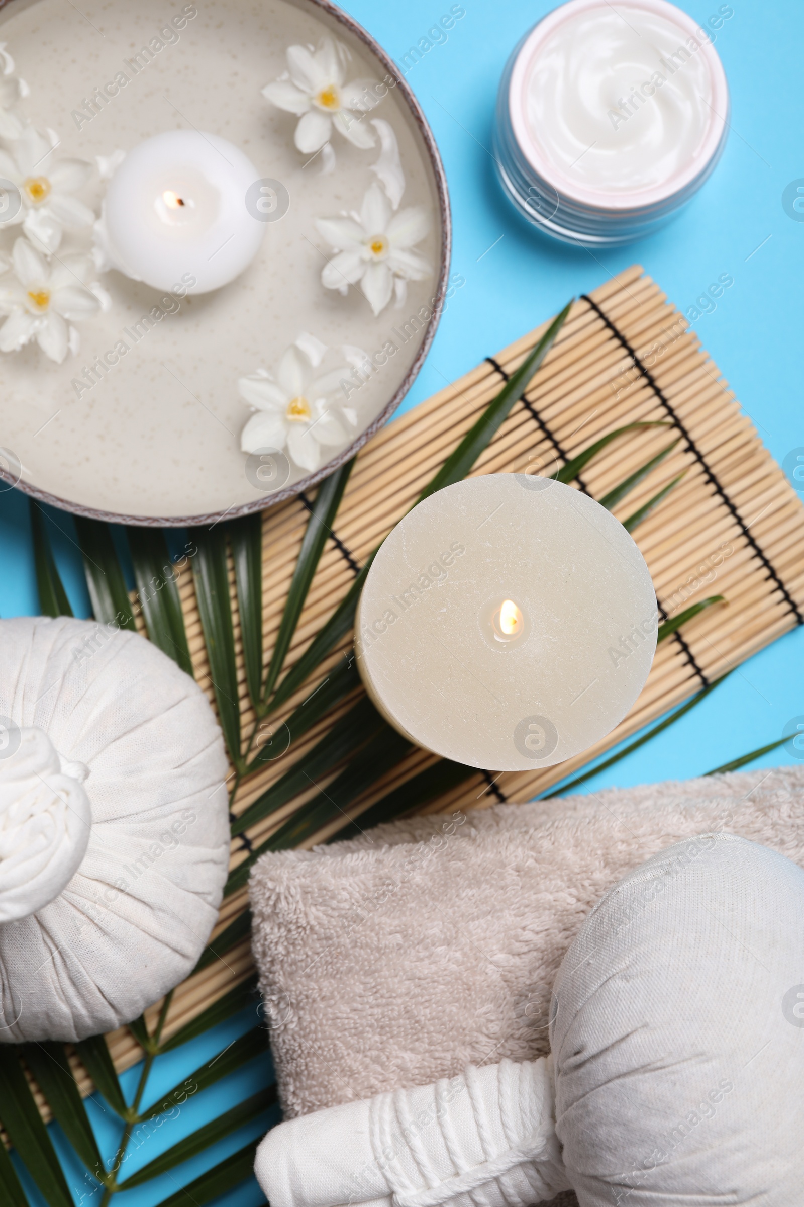 Photo of Flat lay composition with spa products, burning candle and beautiful flowers on light blue background