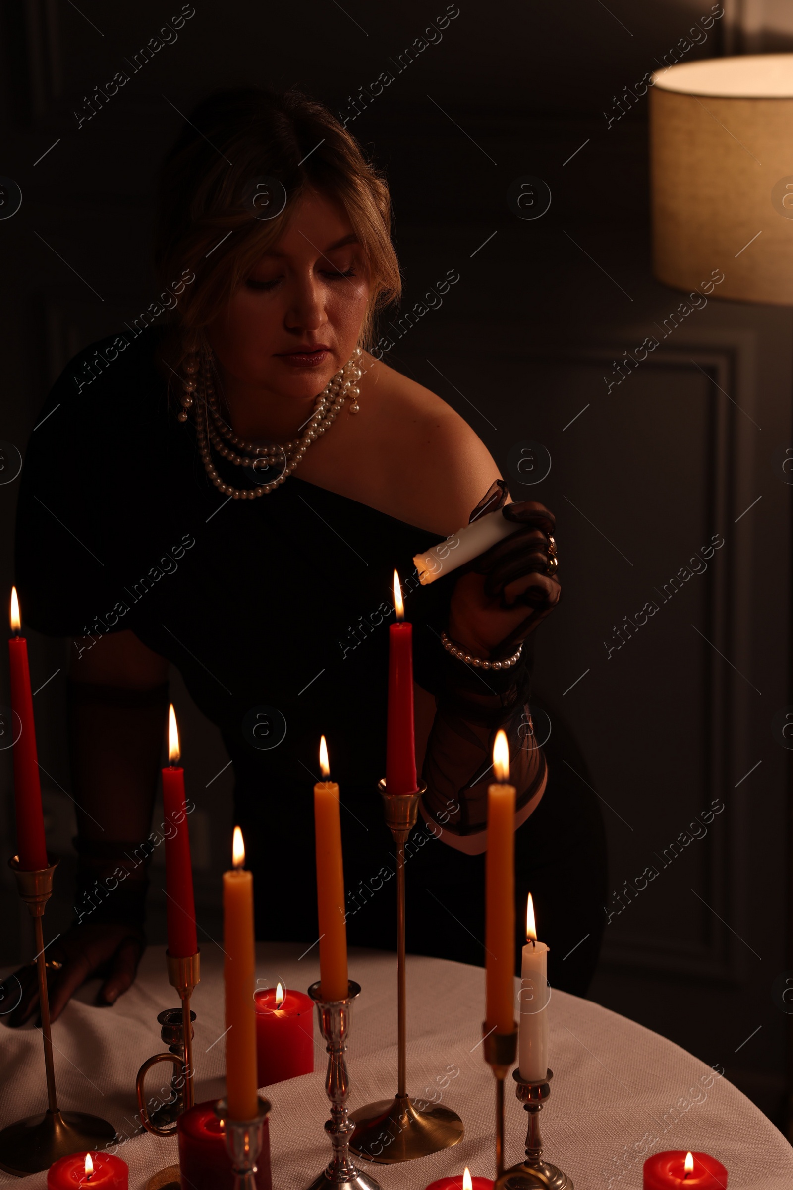 Photo of Beautiful young woman lightning up candle at table indoors