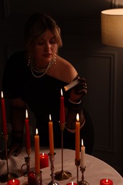 Photo of Beautiful young woman lightning up candle at table indoors