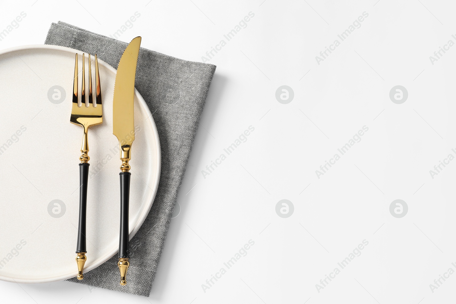 Photo of Stylish golden cutlery, plate and napkin on white background, top view. Space for text