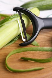 Photo of Fresh cucumber, peels and peeler on wooden board, closeup