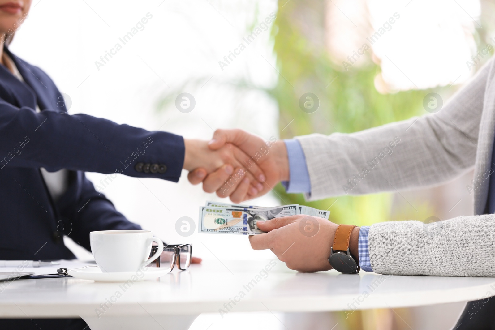 Photo of Man shaking hands with woman and offering bribe at table in office