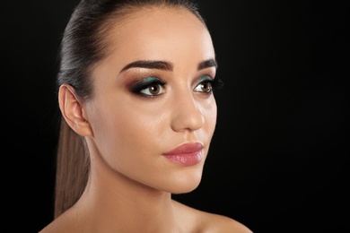 Portrait of young woman with eyelash extensions and beautiful makeup on black background