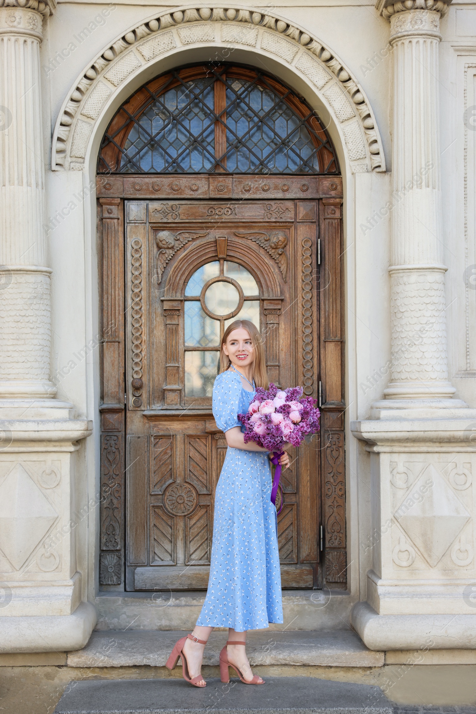 Photo of Beautiful woman with bouquet of spring flowers near building outdoors