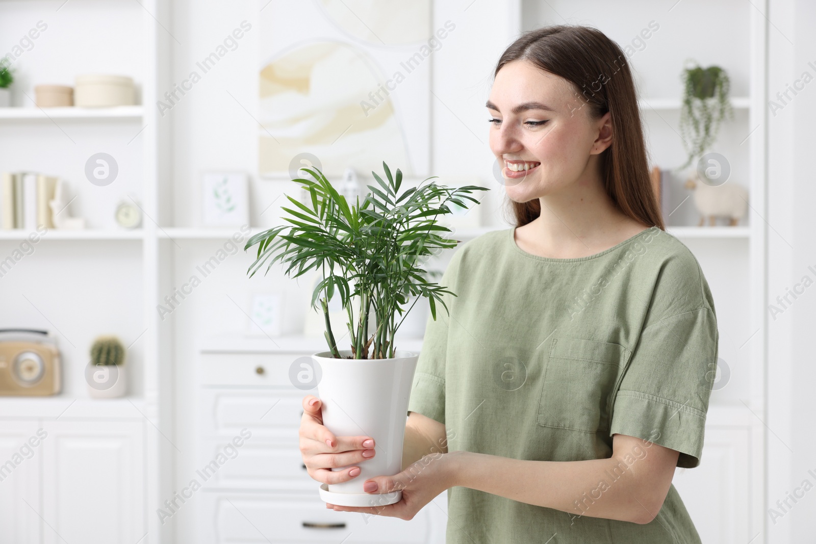 Photo of Beautiful young woman with green houseplant at home, space for text