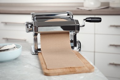 Preparing dough for soba (buckwheat noodles) with pasta maker at light grey table in kitchen