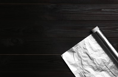 Photo of Roll of aluminum foil on dark wooden table, top view. Space for text