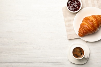 Flat lay composition with cup of coffee and croissant on white wooden background. Space for text