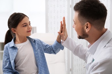 Photo of Pediatrician giving high five to little girl in hospital