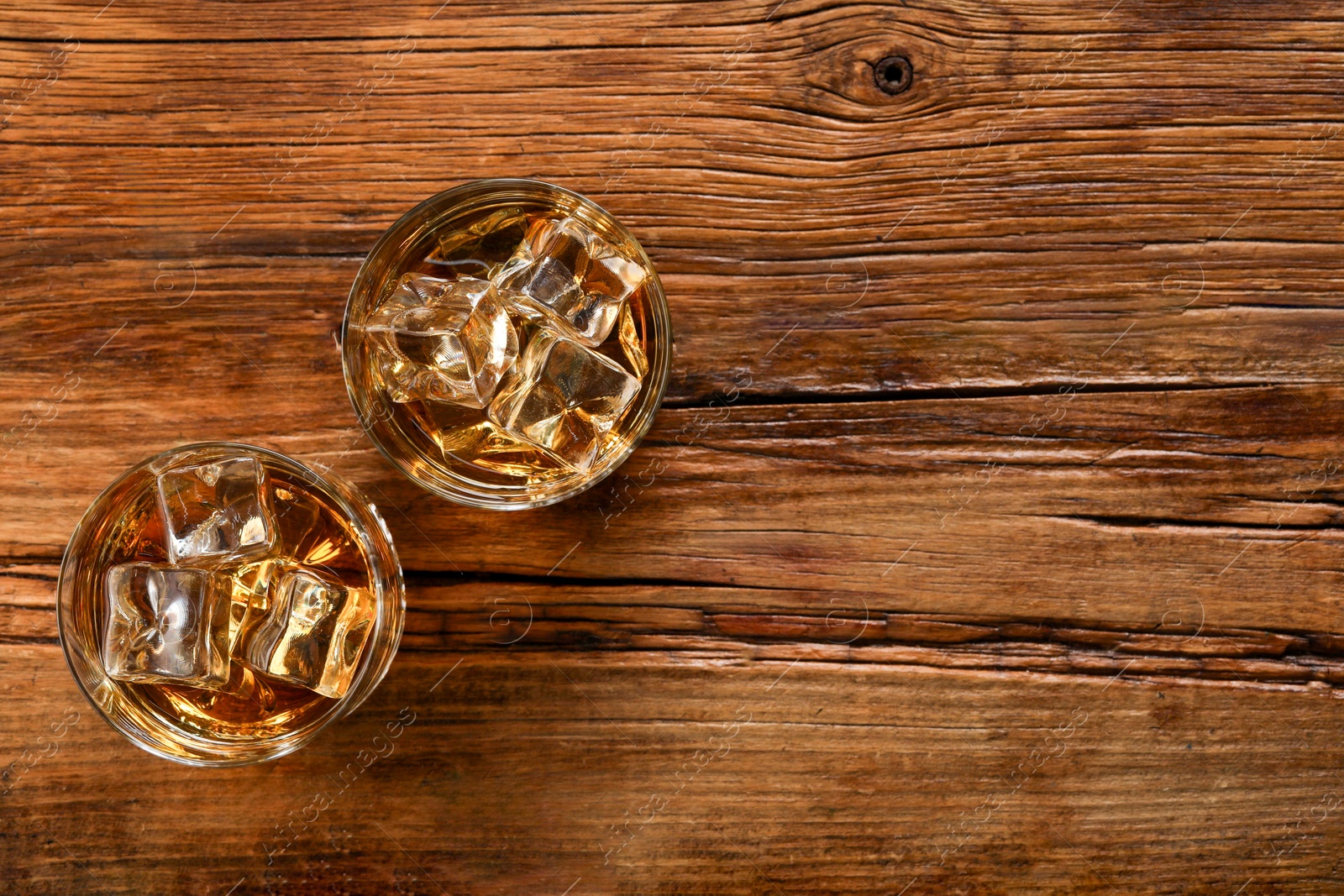 Photo of Whiskey with ice cubes in glasses on wooden table, top view. Space for text