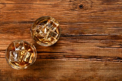 Photo of Whiskey with ice cubes in glasses on wooden table, top view. Space for text