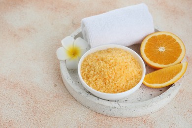 Photo of Sea salt, towel, plumeria flower and cut orange on beige textured table. Space for text