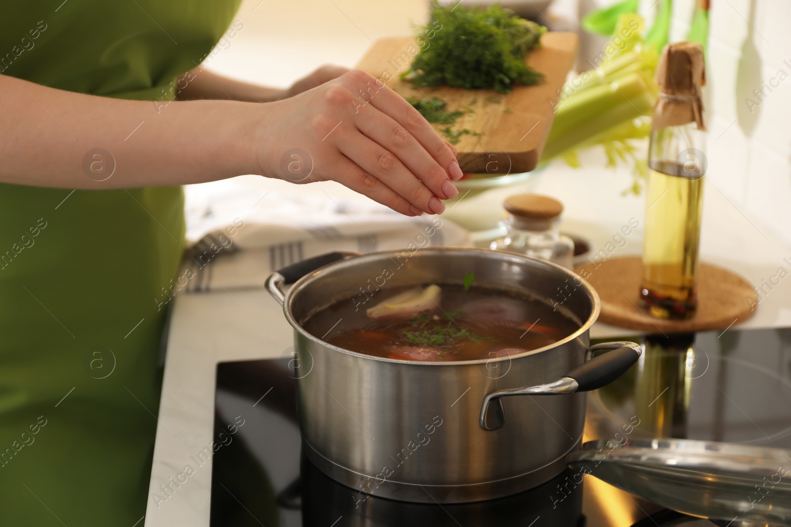 Photo of Woman putting dill into pot to make bouillon in kitchen, closeup. Homemade recipe