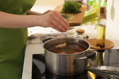 Photo of Woman putting dill into pot to make bouillon in kitchen, closeup. Homemade recipe