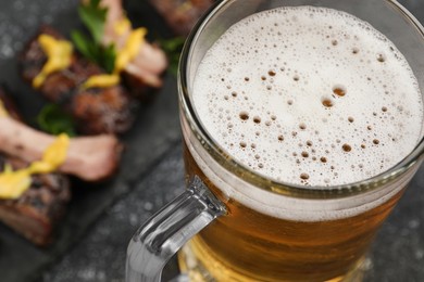Mug with beer and delicious grilled ribs on table, closeup. Space for text